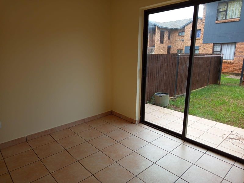 An empty living room featuring ceramic floor tiles and a large sliding glass door providing direct access to the outdoor patio and garden area.