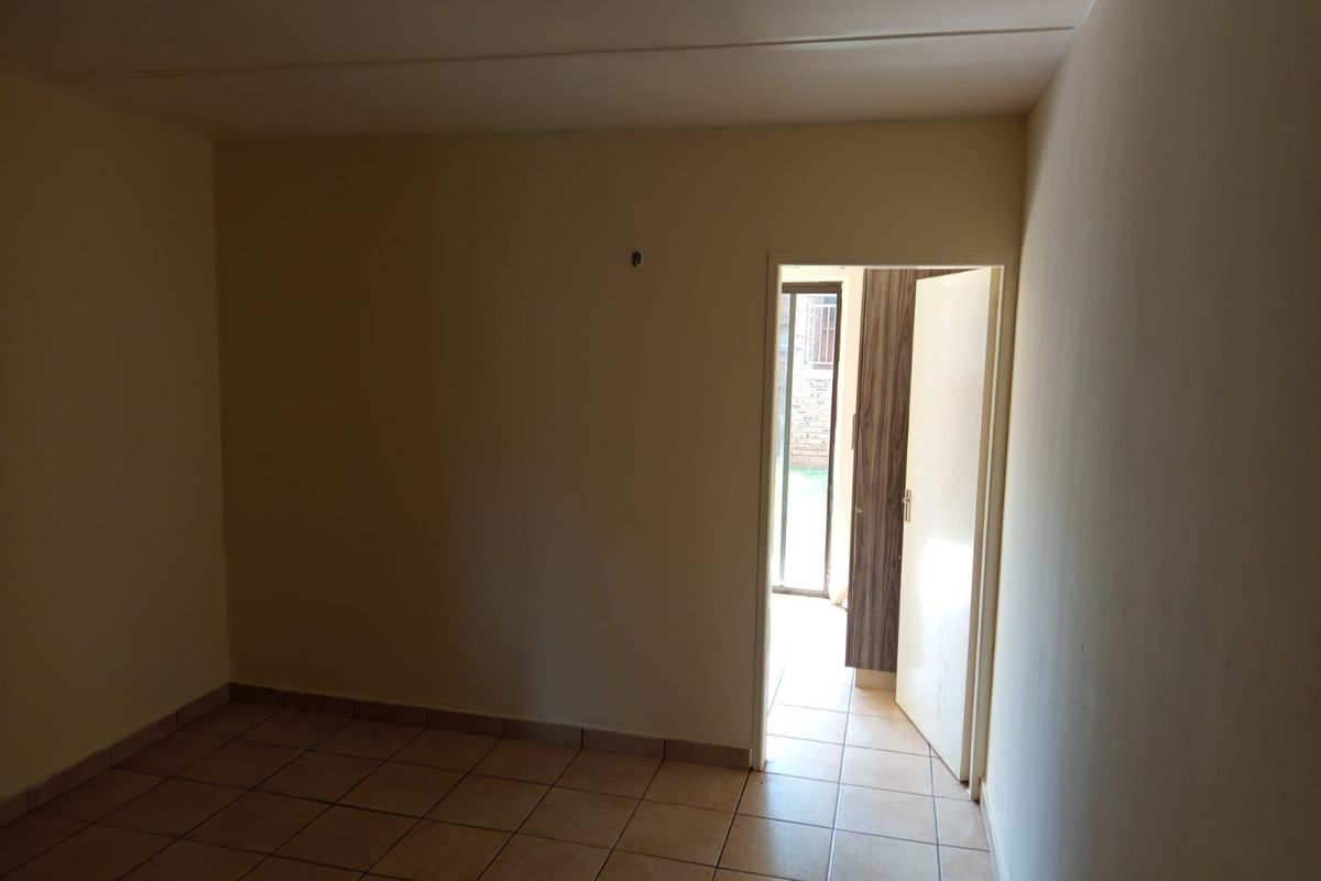 An empty bedroom featuring tiled flooring and a built-in cupboard, with a doorway leading to an exterior area.