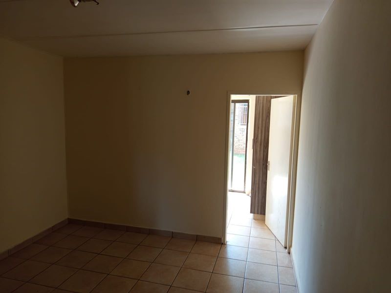 An empty bedroom featuring tiled flooring and a built-in cupboard, with a doorway leading to an exterior area.