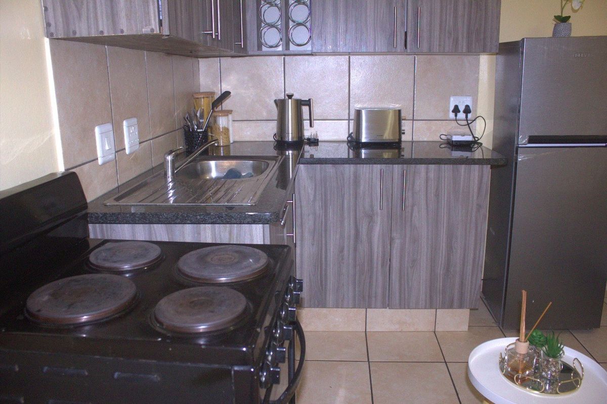 Compact kitchen featuring wood-look laminate cabinetry, granite countertops, a stainless steel sink, and ceramic tile finishes.