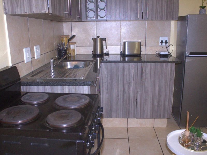 Compact kitchen featuring wood-look laminate cabinetry, granite countertops, a stainless steel sink, and ceramic tile finishes.