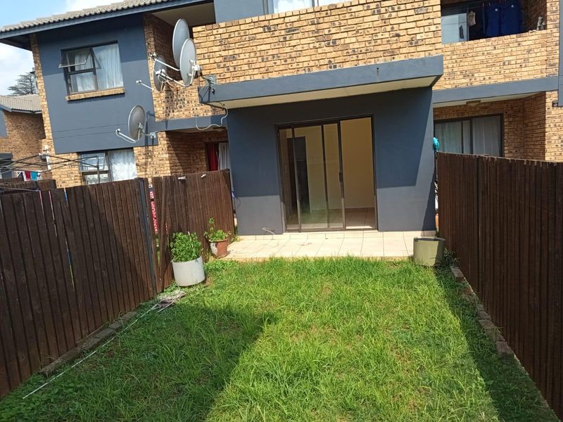 Rear view of the apartment featuring a private garden, wooden fencing, and a tiled patio area accessible through sliding glass doors.