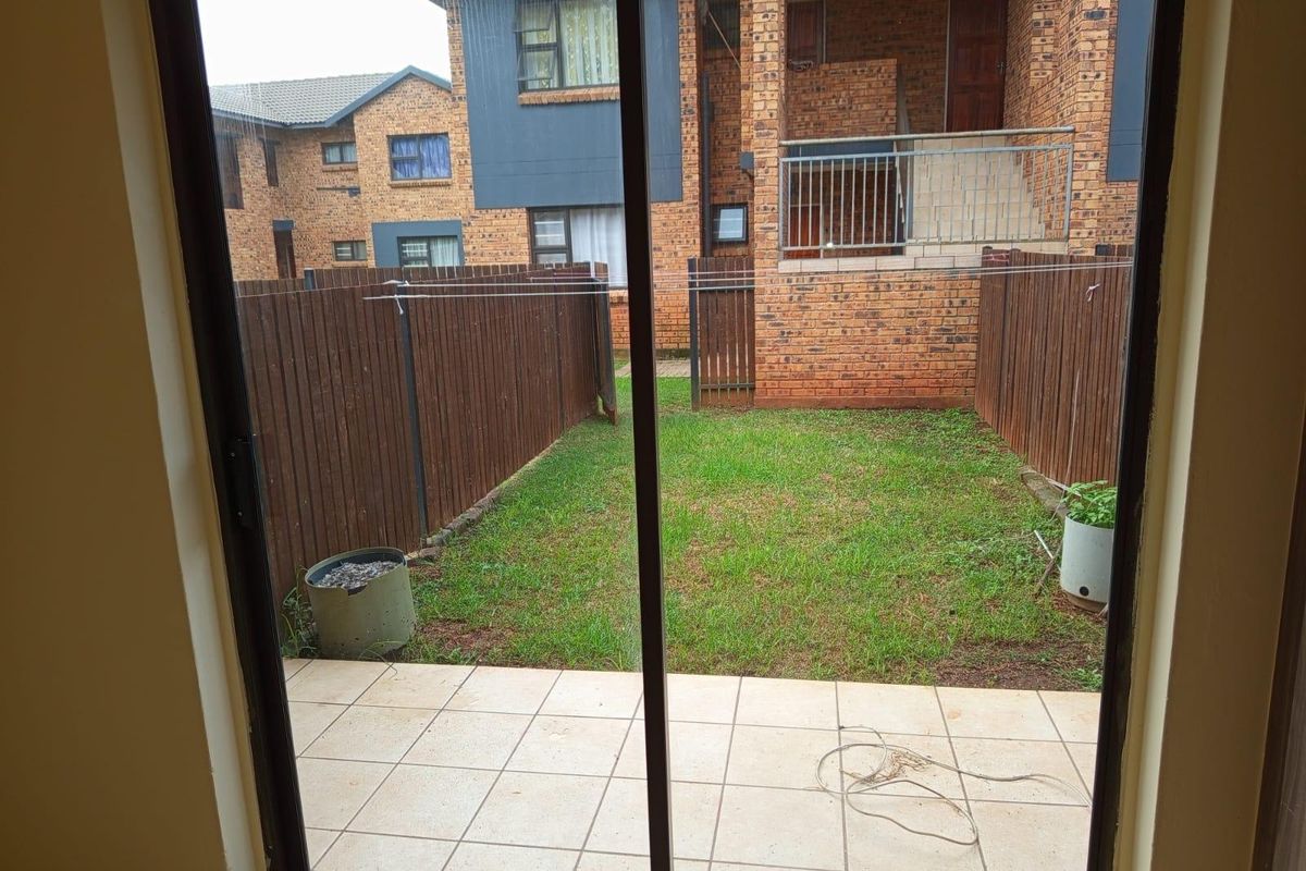 A private rear garden featuring a tiled patio, lawn area, and timber fencing, viewed through a sliding glass door.