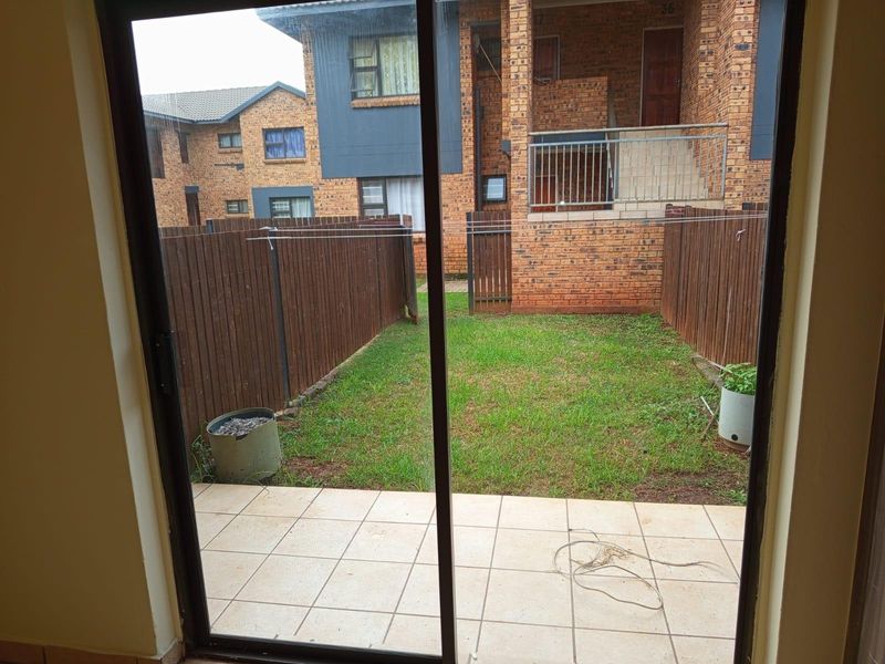A private rear garden featuring a tiled patio, lawn area, and timber fencing, viewed through a sliding glass door.