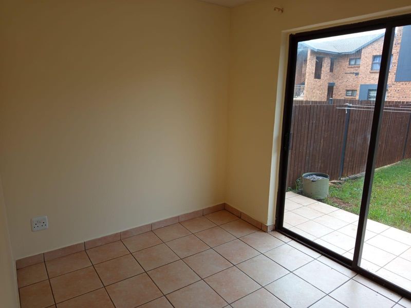 An empty living area featuring ceramic floor tiles and a sliding glass door providing direct access to the outdoor patio and garden.