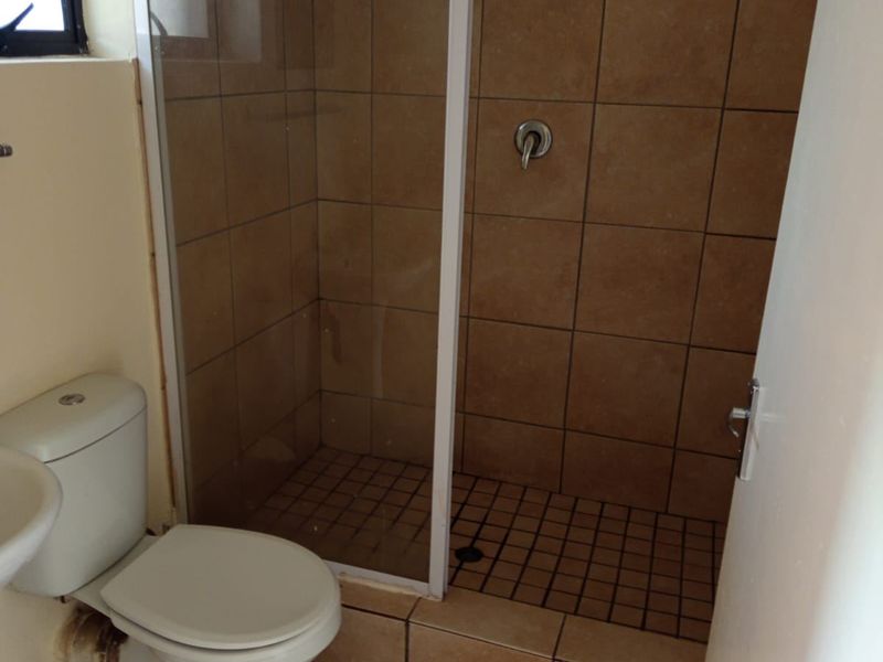 A functional bathroom featuring a tiled shower enclosure, standard toilet, and wash basin with neutral floor tiling.