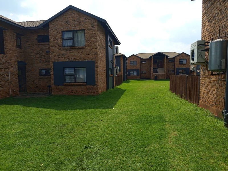 A view of the rear exterior of the apartment complex, featuring face brick facades, communal lawn space, and established boundary fencing.