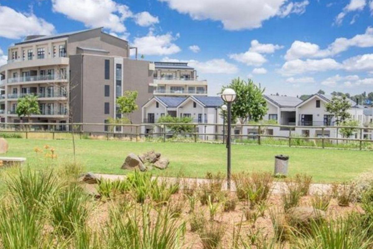 A view of the landscaped communal garden area featuring a pathway, post and rail fencing, and exterior lighting within the apartment complex grounds.