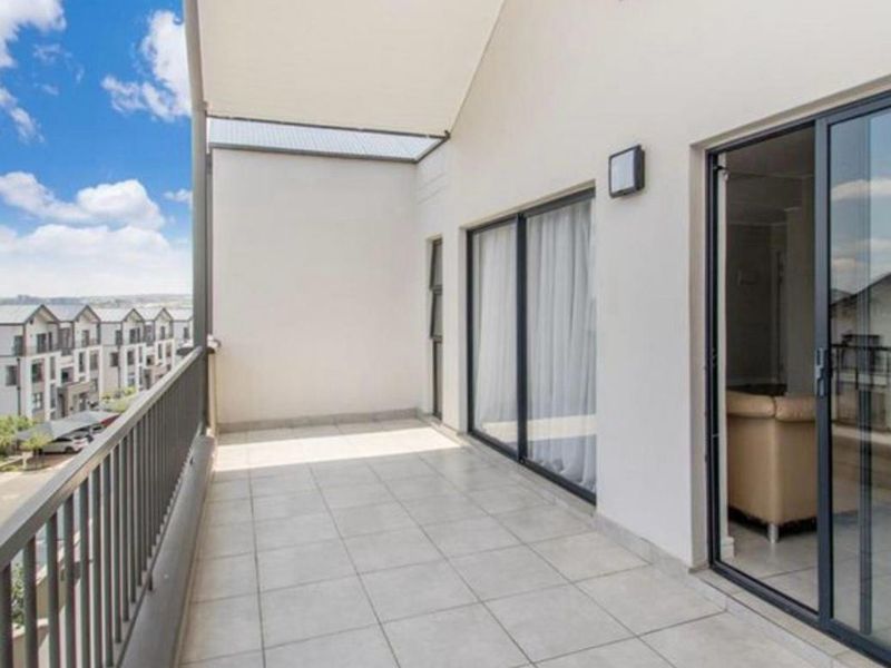 A spacious, covered balcony featuring tiled flooring, a metal balustrade, and sliding glass door access to the interior living area.