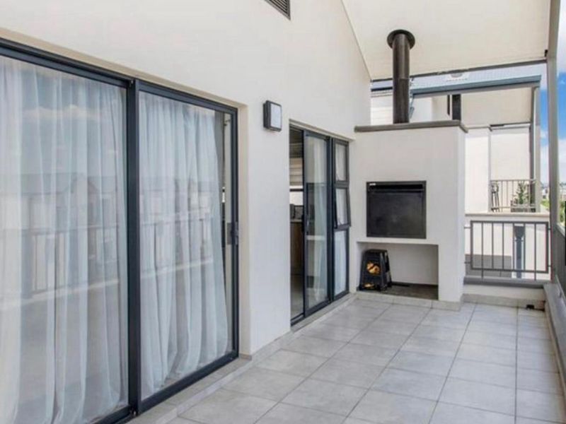 A spacious covered balcony featuring tiled flooring, a built-in braai, and large sliding glass doors providing seamless indoor-outdoor flow.