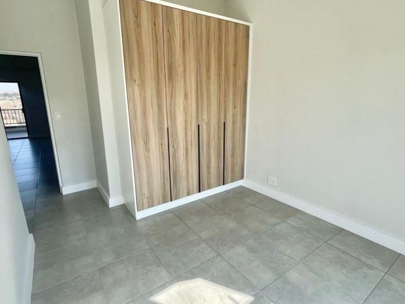 A bright, modern bedroom featuring neutral walls, large-format grey floor tiles, and contemporary wood-finish built-in cupboards.