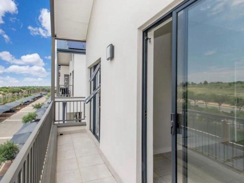 A clean, modern balcony featuring tiled flooring, a metal balustrade, and sliding glass door access to the interior.