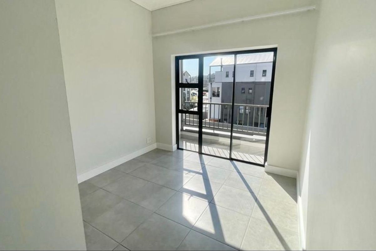 A bright, empty bedroom featuring neutral tiled flooring and a sliding glass door that provides direct access to a private balcony.