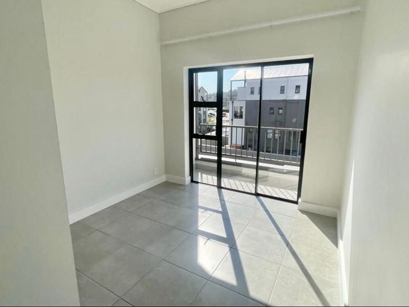A bright, empty bedroom featuring neutral tiled flooring and a sliding glass door that provides direct access to a private balcony.