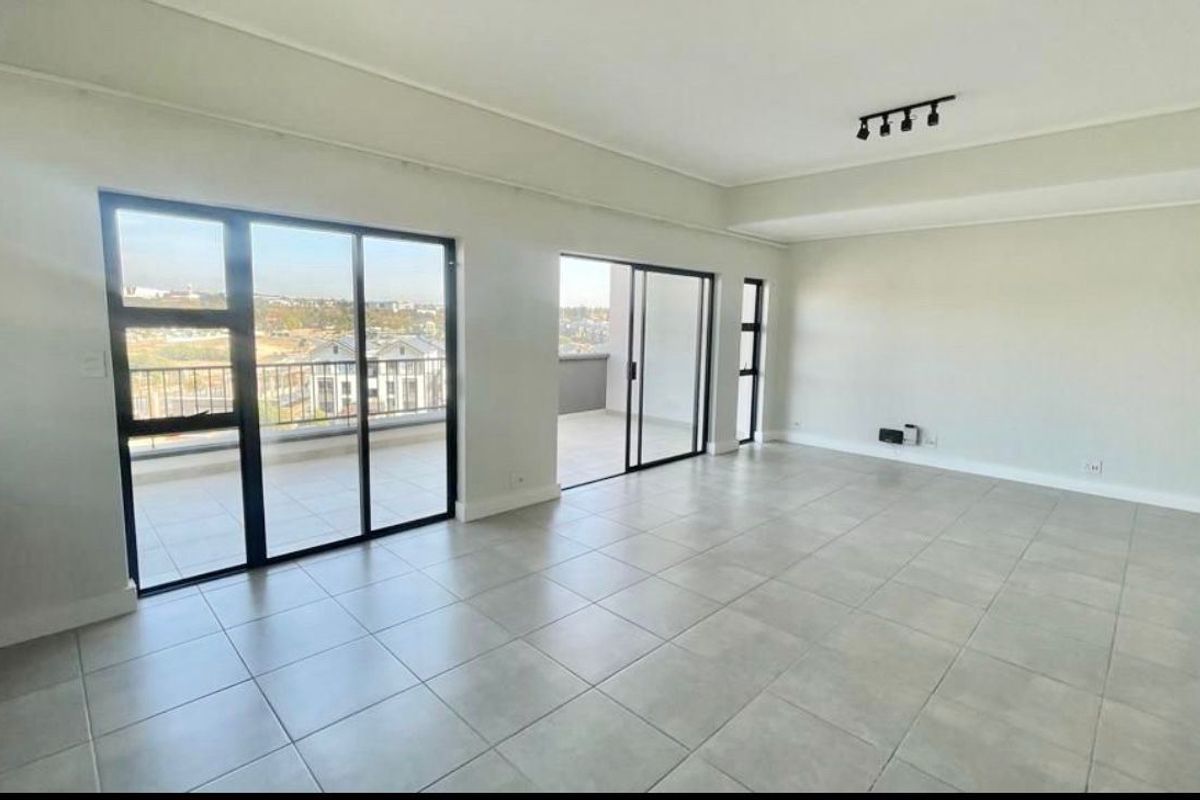 Spacious, light-filled open plan living area featuring neutral tiled flooring, modern recessed lighting, and large sliding glass doors leading to a private balcony.