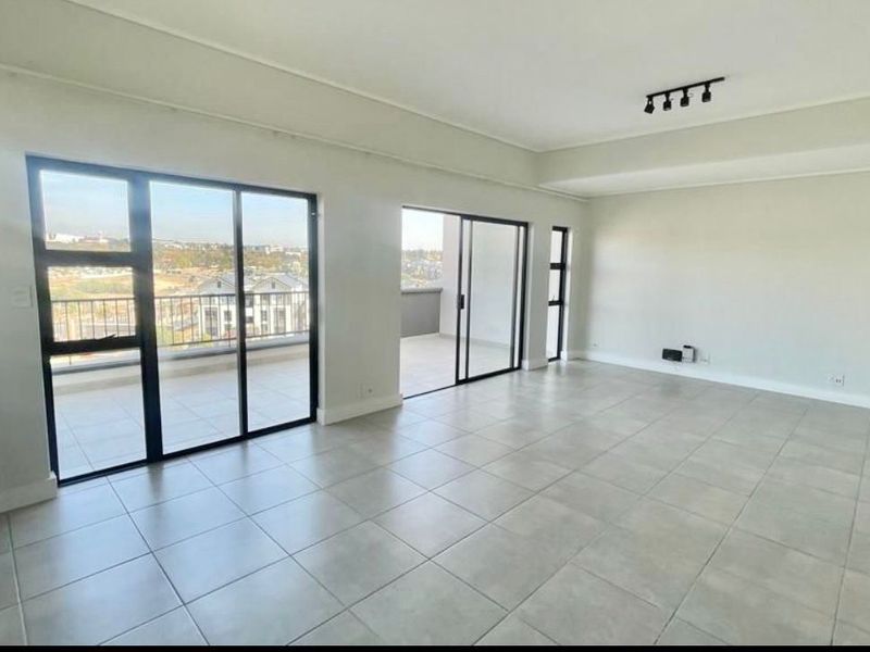 Spacious, light-filled open plan living area featuring neutral tiled flooring, modern recessed lighting, and large sliding glass doors leading to a private balcony.