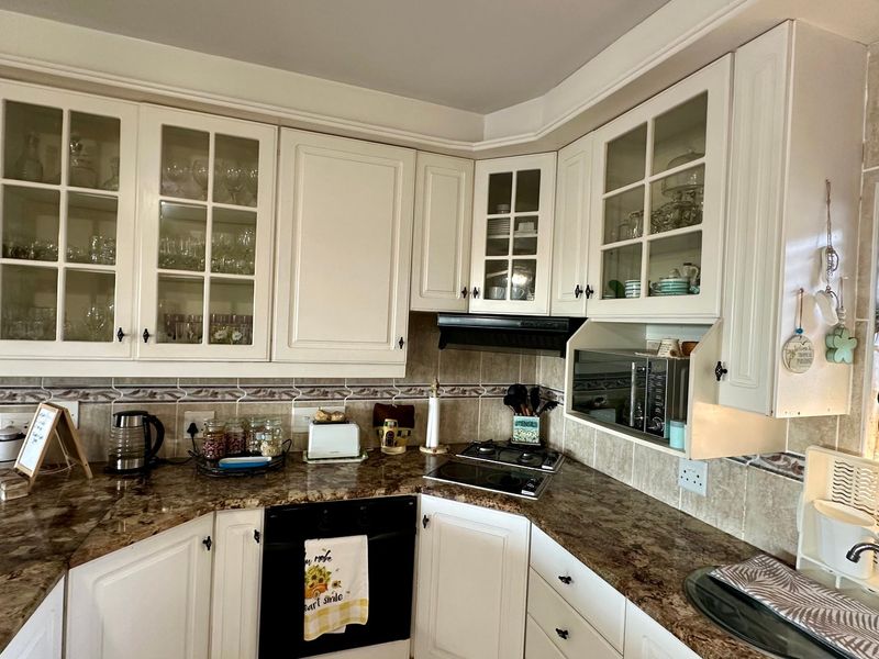 A functional kitchen featuring white cabinetry, granite countertops, a tiled backsplash, and integrated appliances including an oven and cooktop.
