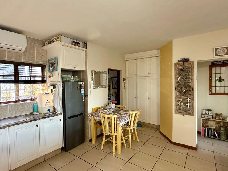 Functional kitchen featuring built-in cabinetry, laminate countertops, tiled flooring, and integrated pantry storage, with a wall-mounted air conditioning unit for climate control.