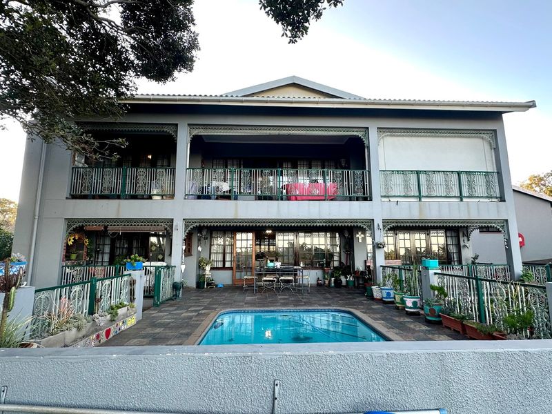 Rear view of a double-story townhouse featuring a swimming pool, paved patio area, and upper-level balconies with decorative wrought iron railings.