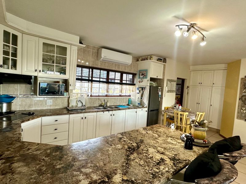 Open-plan kitchen featuring granite countertops, ample built-in cabinetry, a double basin sink, and a wall-mounted air conditioning unit.