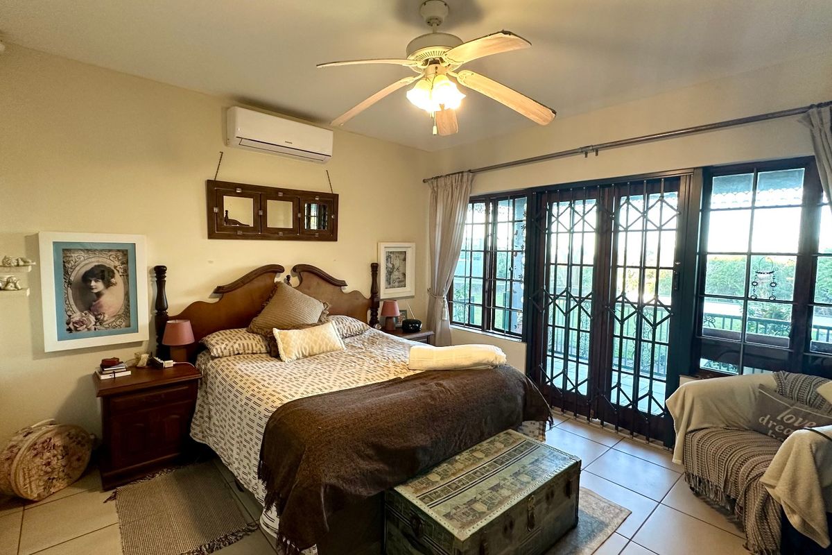 Spacious bedroom featuring tiled flooring, a ceiling fan, split-system air conditioning, and direct access to an outdoor area through sliding glass doors with security gates.