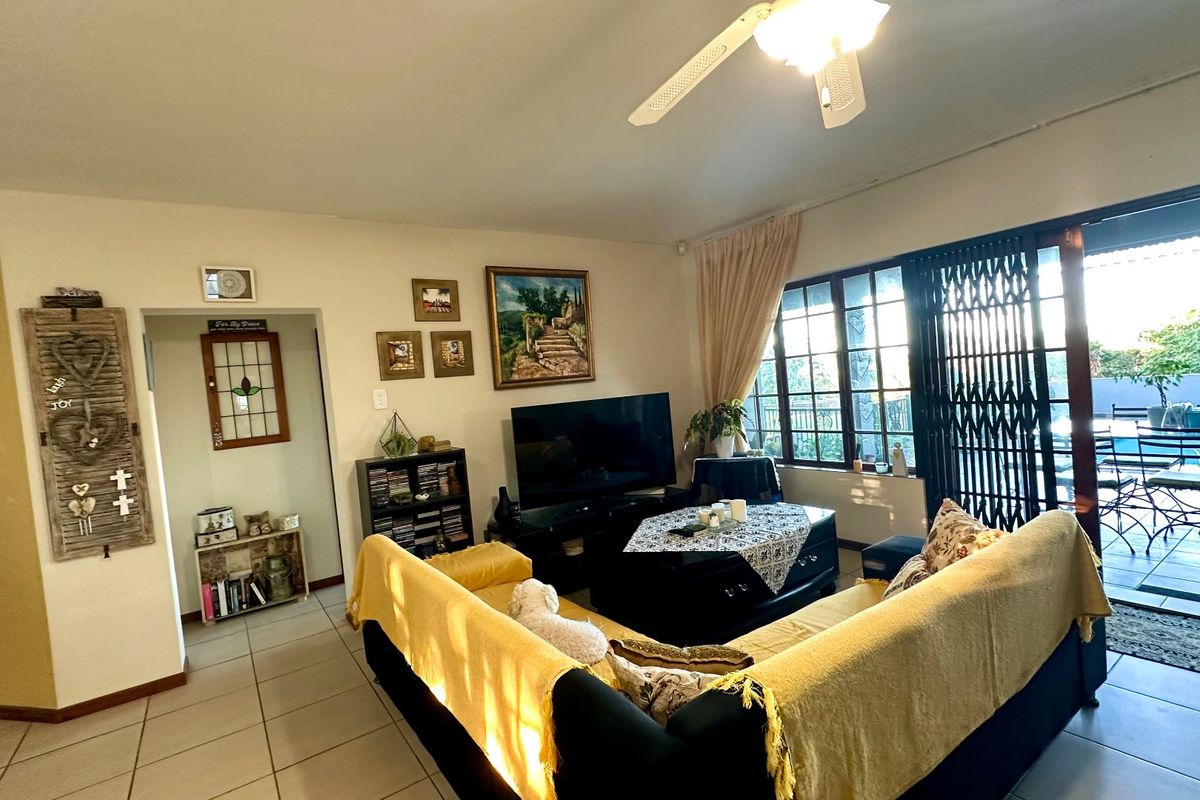 A living room featuring tiled flooring, a ceiling fan, and large sliding glass doors with security gates leading to an outdoor patio area.