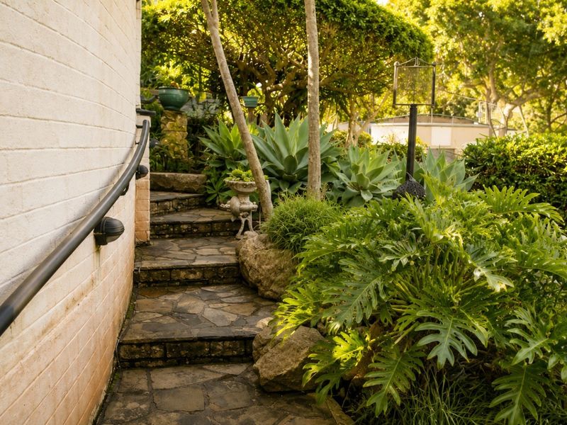 A charming garden pathway featuring stone steps, a sturdy metal handrail, and lush established greenery leading through the property's outdoor space.
