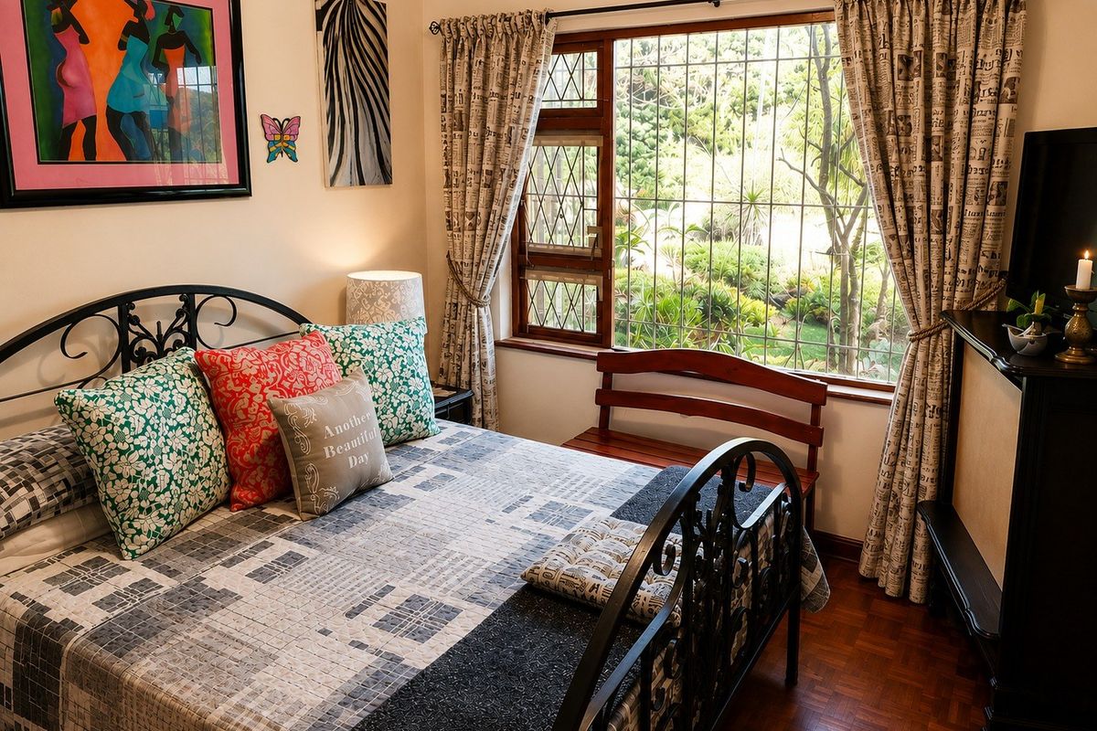 A cozy bedroom featuring warm parquet flooring and a large window with security bars, offering a pleasant view of the garden.