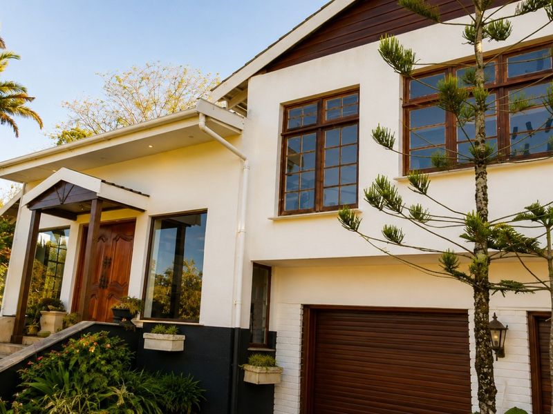 Front elevation of a multi-level home featuring a double garage, timber-framed windows, and a prominent timber entrance door with landscaped garden surrounds.