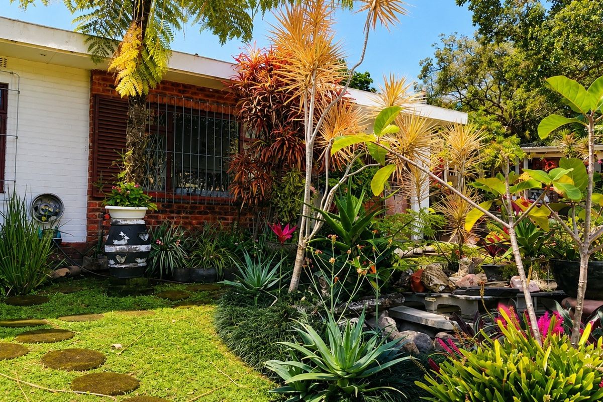 A lush rear garden featuring a brick facade, established tropical landscaping, and a stone water feature.