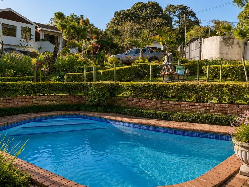 A well-maintained swimming pool area featuring brick coping, tiered landscaped gardens, and established hedging in a sunny outdoor setting.