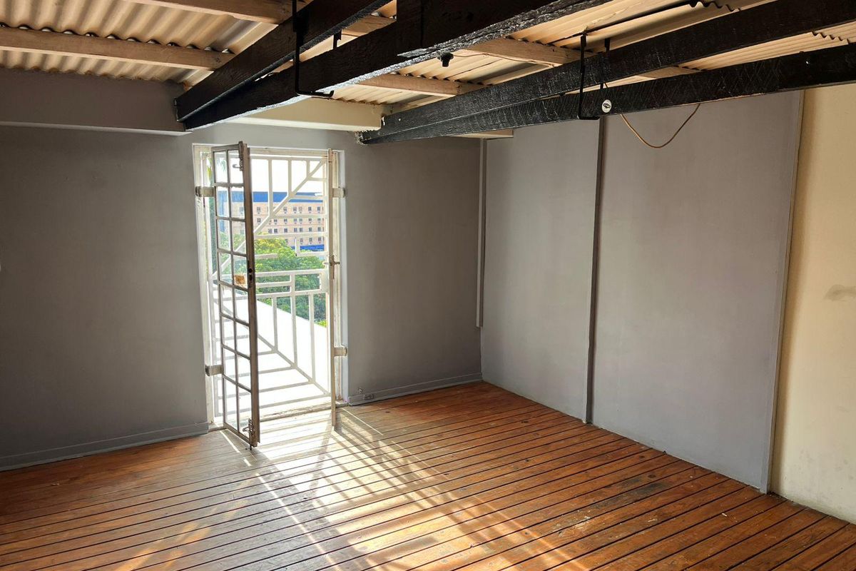 An empty bedroom featuring exposed timber ceiling beams, timber slat flooring, and a security gate leading to an exterior balcony.
