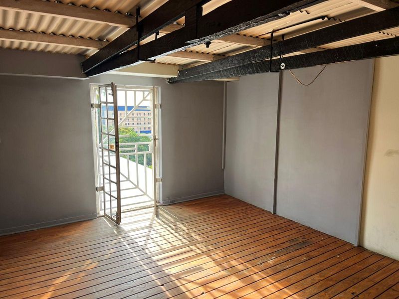 An empty bedroom featuring exposed timber ceiling beams, timber slat flooring, and a security gate leading to an exterior balcony.