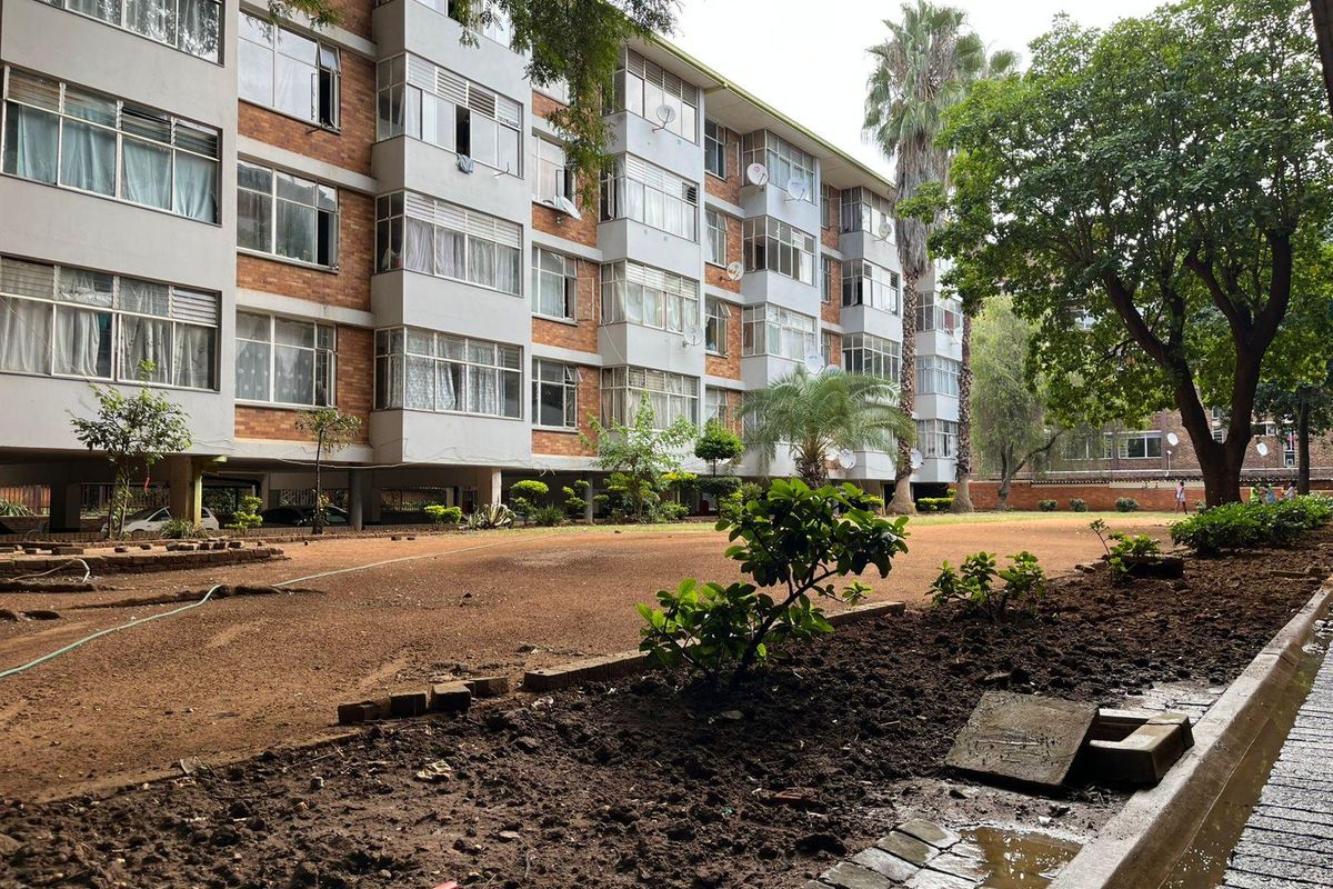 Exterior view of an apartment building featuring a brick facade, aluminium windows, and a shared garden area with paved walkways.