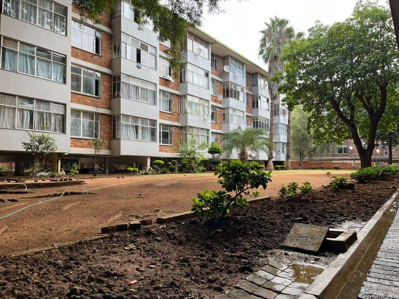 Exterior view of an apartment building featuring a brick facade, aluminium windows, and a shared garden area with paved walkways.