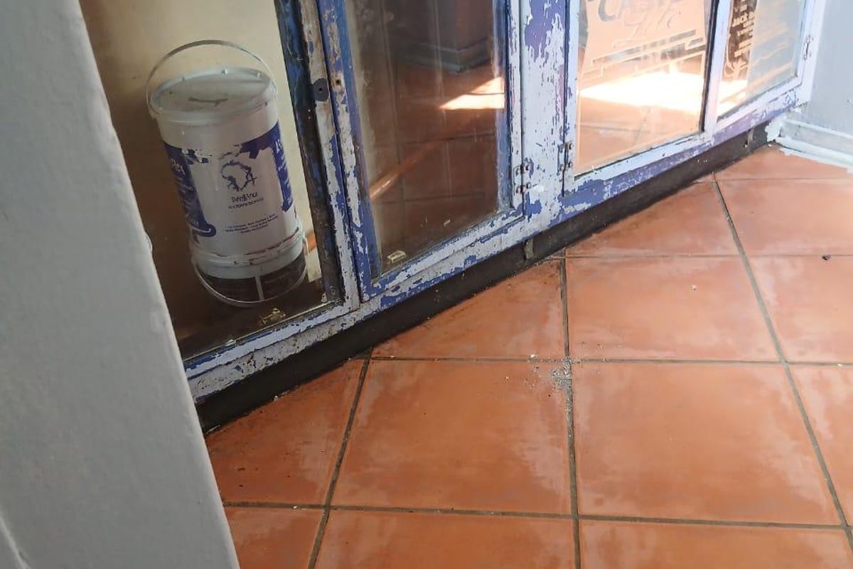 A kitchen area featuring built-in cabinetry with glass-panel doors and terracotta-style ceramic floor tiles, currently showing significant wear and peeling paint.