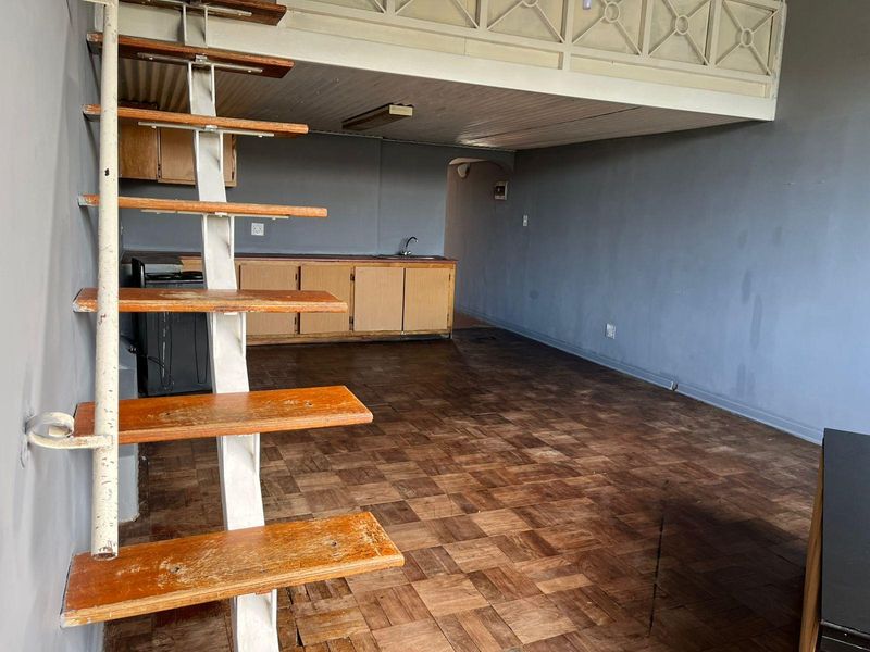 Open-plan living area featuring a mezzanine level, parquet flooring, and a basic kitchenette with built-in cabinetry.