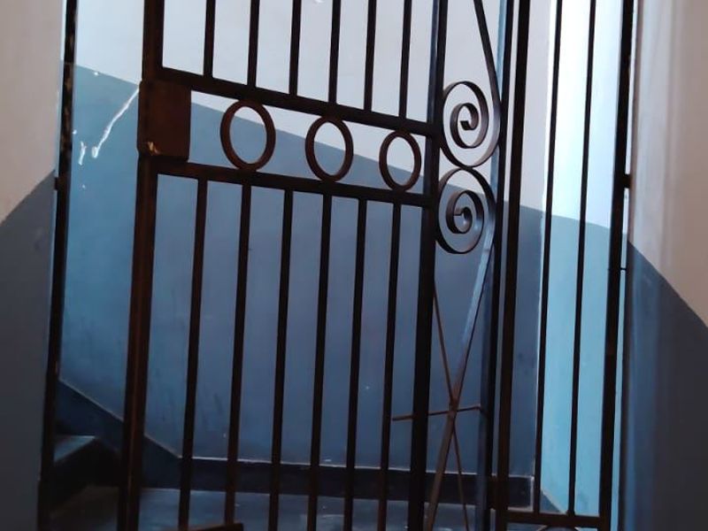 An interior entry area featuring a metal security gate and staircase with visible wear on the wall finishes.