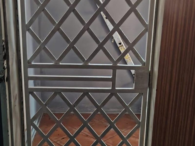 A view through a white metal security gate into a small tiled entryway.