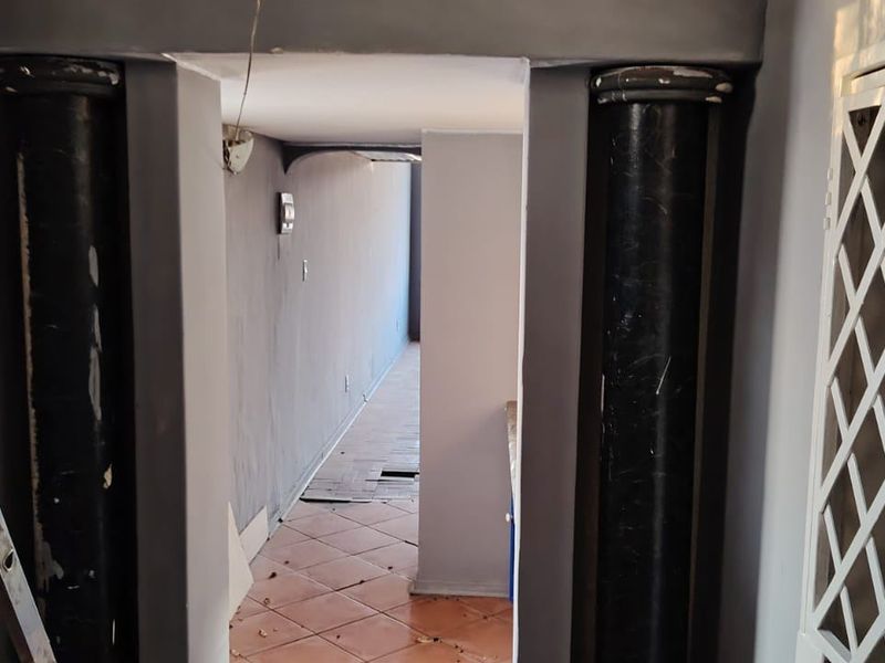 A narrow hallway featuring structural columns and tiled flooring, currently in need of cosmetic repairs and finishing to improve its overall condition.