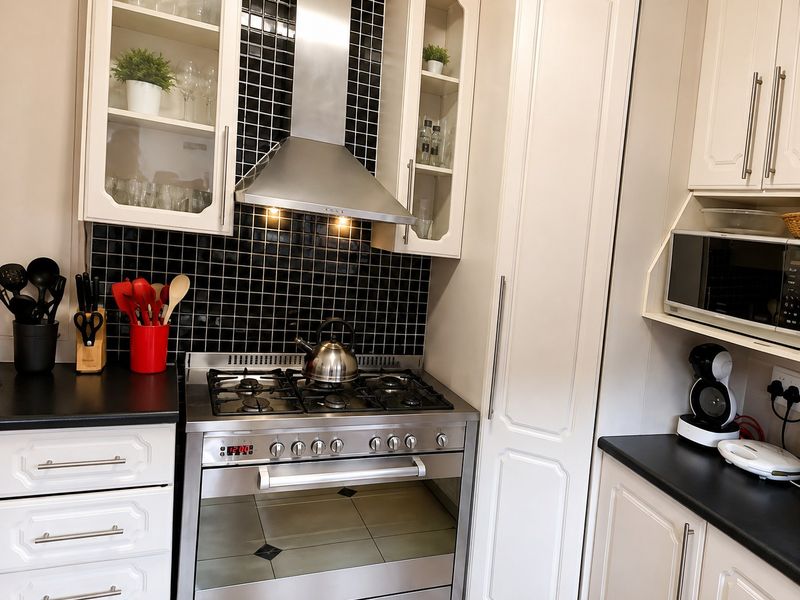 A well-maintained kitchen featuring a stainless steel gas stove, extractor fan, built-in cabinetry, and a contrasting black tiled backsplash.