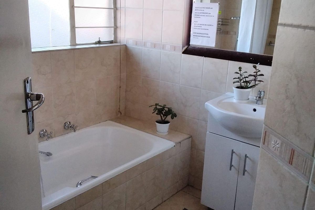 A functional bathroom featuring a built-in bathtub, vanity cabinet with basin, and tiled finishes throughout, providing a practical space for daily use.