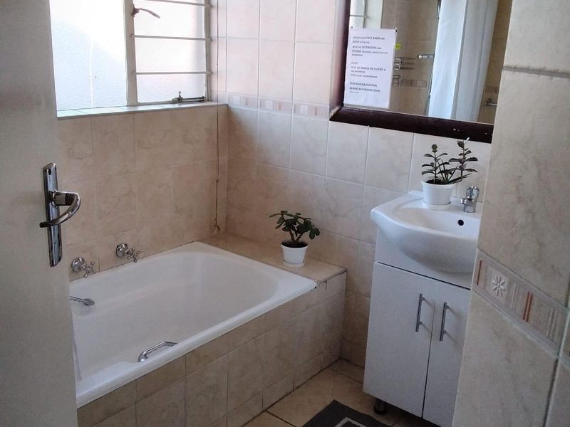 A functional bathroom featuring a built-in bathtub, vanity cabinet with basin, and tiled finishes throughout, providing a practical space for daily use.