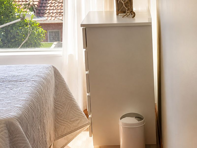 A bright bedroom featuring laminate flooring and a large window providing natural light and a view of the surrounding neighborhood.