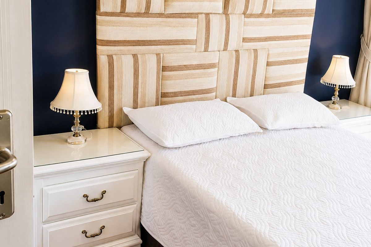A well-maintained bedroom featuring hardwood flooring and a large, custom-upholstered headboard against a dark accent wall.