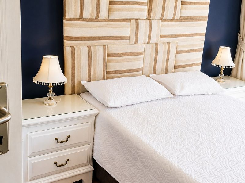 A well-maintained bedroom featuring hardwood flooring and a large, custom-upholstered headboard against a dark accent wall.