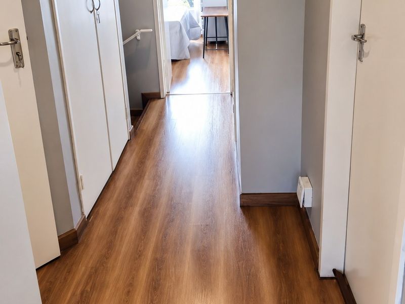 A clean, well-maintained hallway featuring wood-look laminate flooring and built-in storage cupboards, providing access to adjacent rooms.
