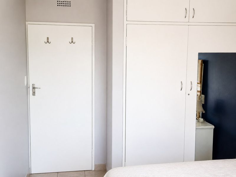 A bedroom interior featuring white built-in cupboards with overhead storage and a standard door with wall-mounted hooks.
