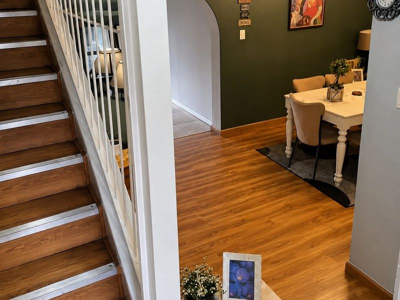 A view of a living area featuring wood-look laminate flooring, a staircase with a metal balustrade, and an arched entryway leading to another space.