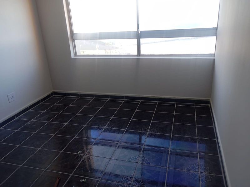 An empty bedroom featuring dark tiled flooring and a large window providing natural light.